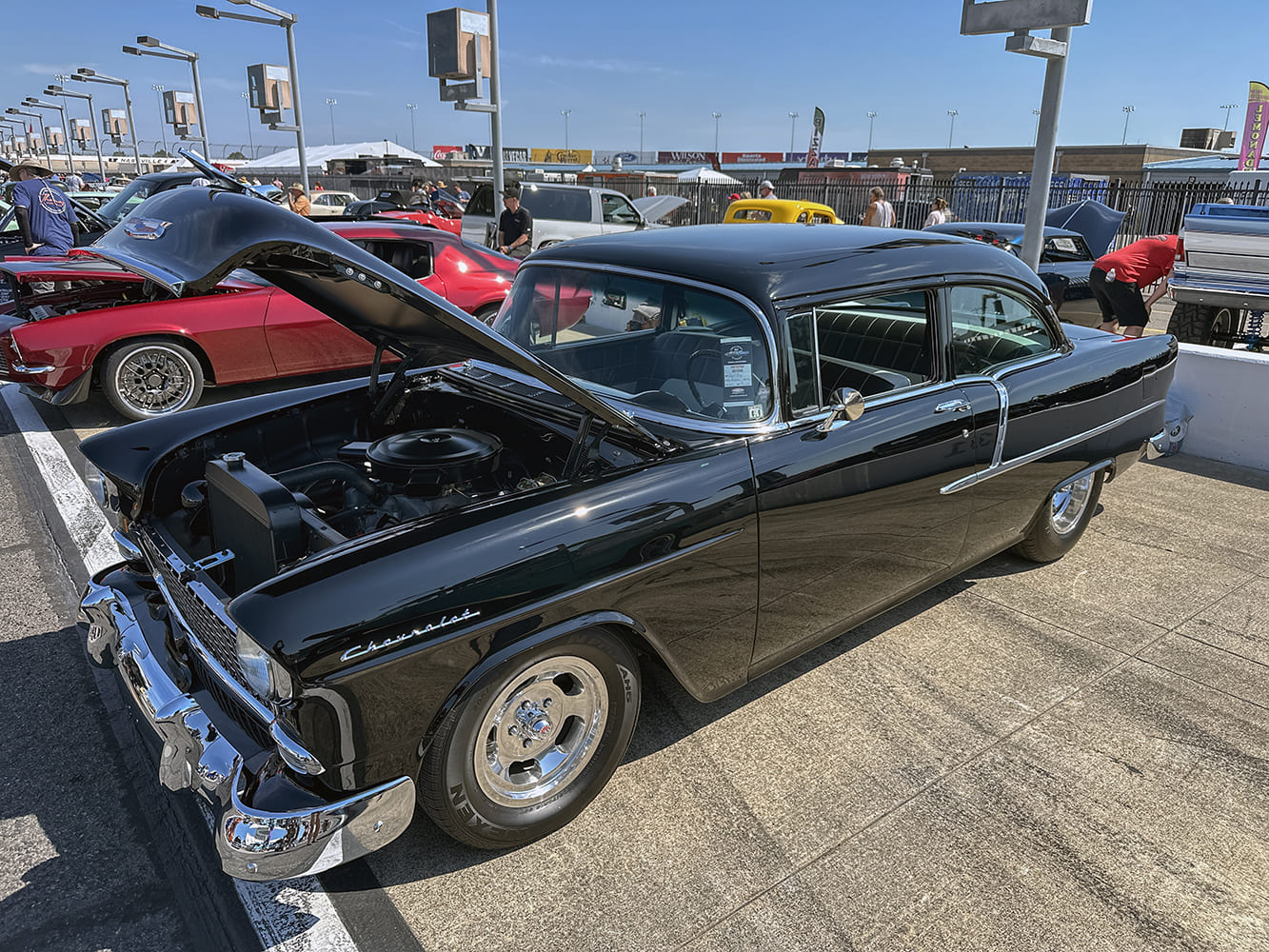 High front three-quarter view of a jet black 1956 Chevrolet 210 sedan showing an open engine bay and polished American Racing Torq Thrust wheels.