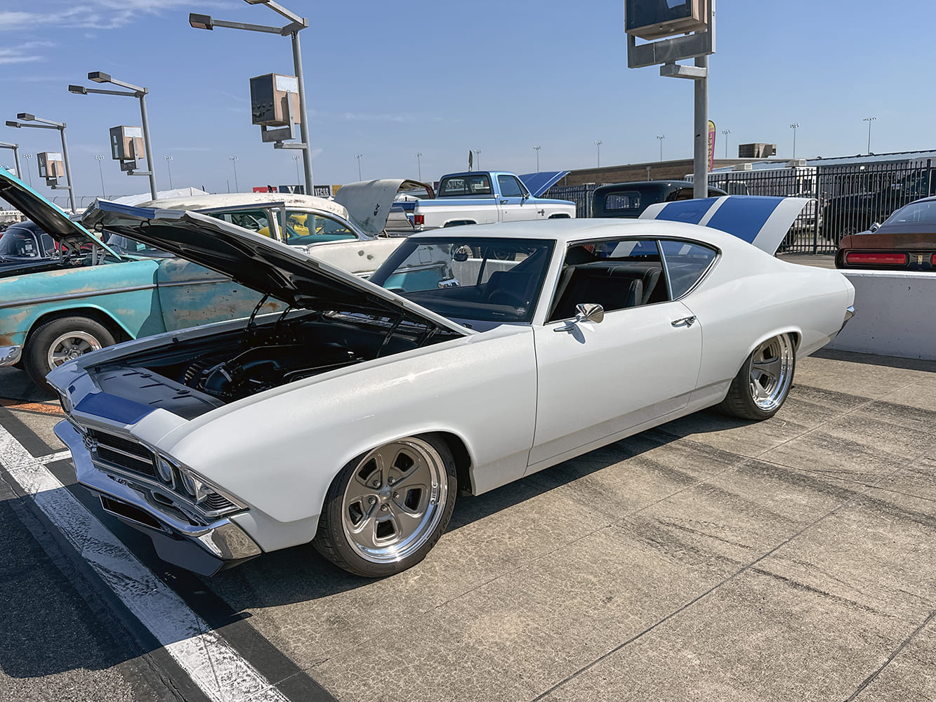 Front three-quarter perspective of a white 1968 Chevrolet Chevelle SS with an open cowl-induction hood, blue stripes, and bronze alloy wheels.