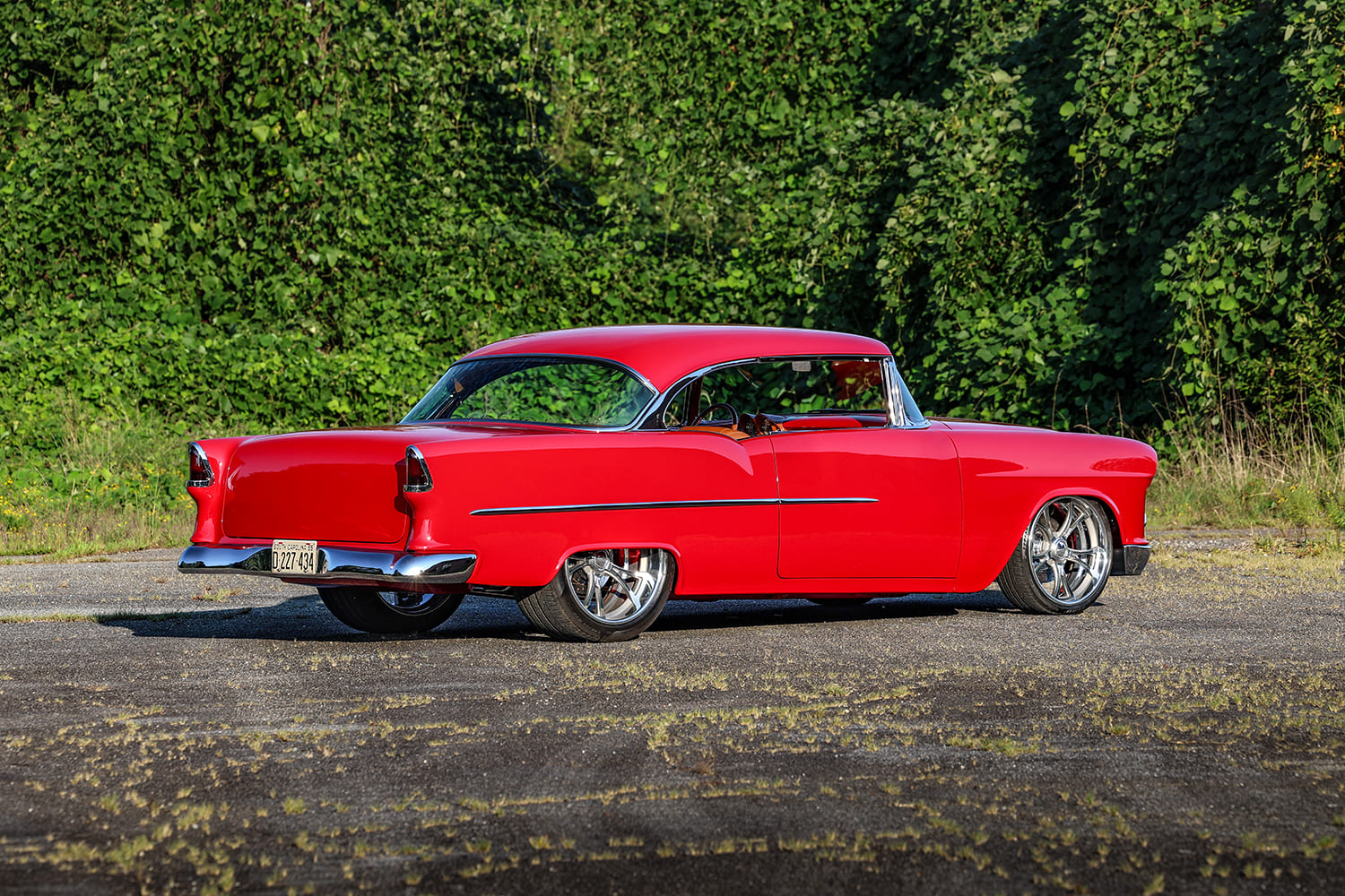 Rear three-quarter view of a custom bright red 1955 Bel Air showing chrome bumper and tucked aftermarket wheels.
