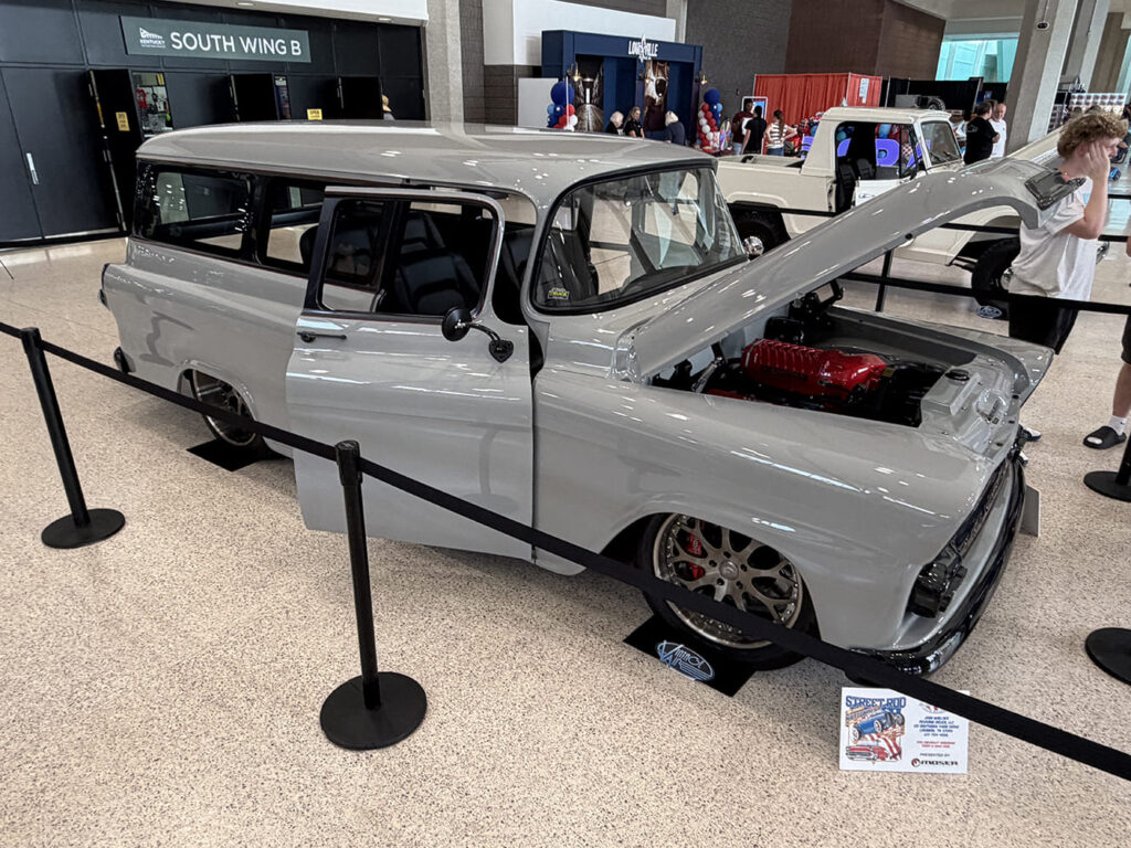 Front three-quarter angle of a light battleship gray 1950s Ford two-door wagon restomod with an open hood showcasing a red supercharger on custom wheels.