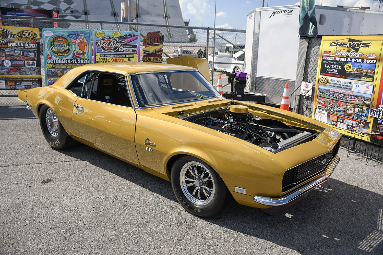 Front three-quarter angle of a metallic gold 1968 Chevrolet Camaro SS pro-street drag car with an open hood and polished racing wheels.