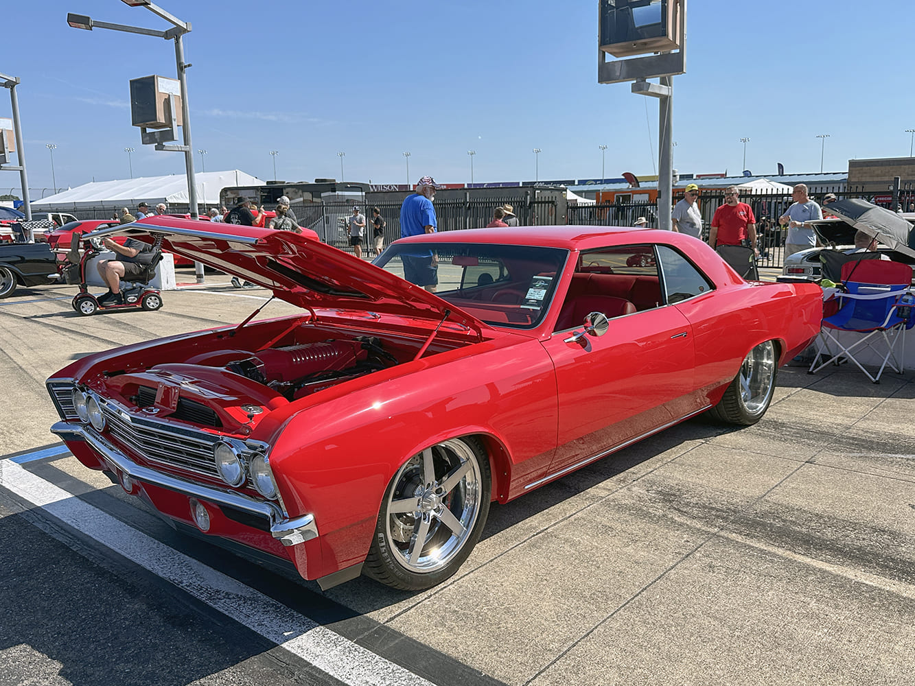 Low front three-quarter view of a bright red 1966 Chevrolet Chevelle hardtop with an open hood showing an LT V8 engine and polished five-spoke wheels