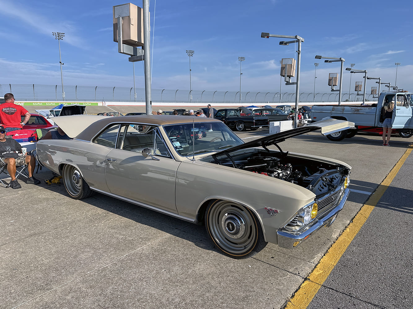 Front three-quarter perspective of a lowered beige 1966 Chevrolet Chevelle with a brown roof, open hood, and color-matched steel-style wheels.