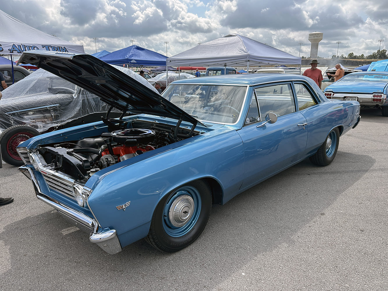 Front three-quarter view of a classic medium blue 1966 Chevrolet Chevelle post coupe with an open hood, stock engine bay, and dog-dish hubcaps