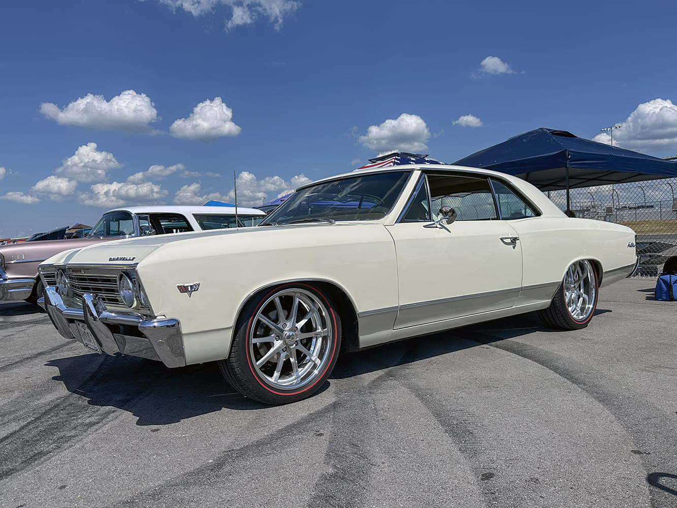 Low-angle front three-quarter view of an off-white 1966 Chevrolet Chevelle sport coupe with polished multi-spoke wheels and thin redline performance tires.