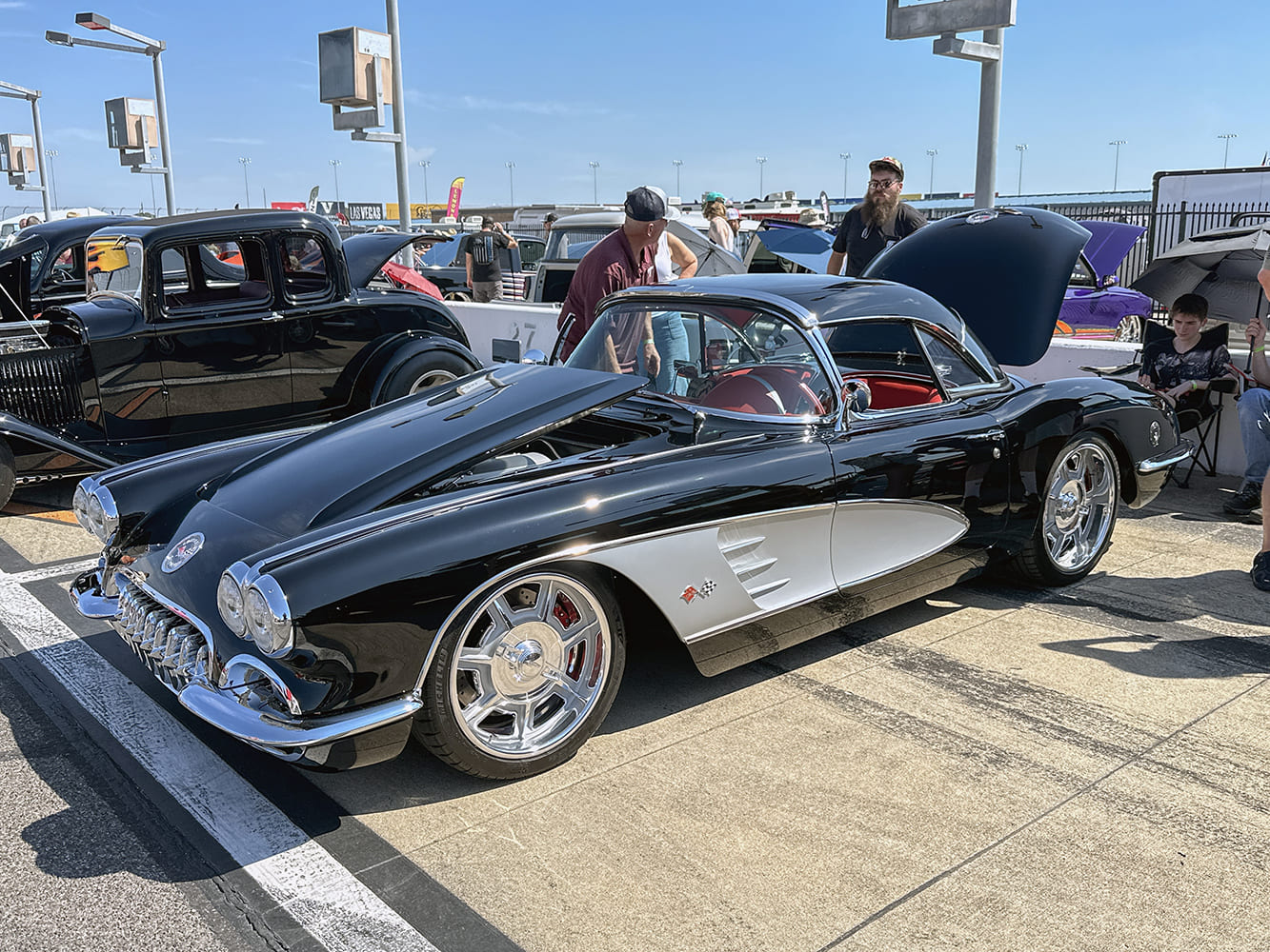 High front three-quarter view of a black 1959 Chevrolet Corvette with silver coves, red interior, hardtop, and modern large billet wheels.