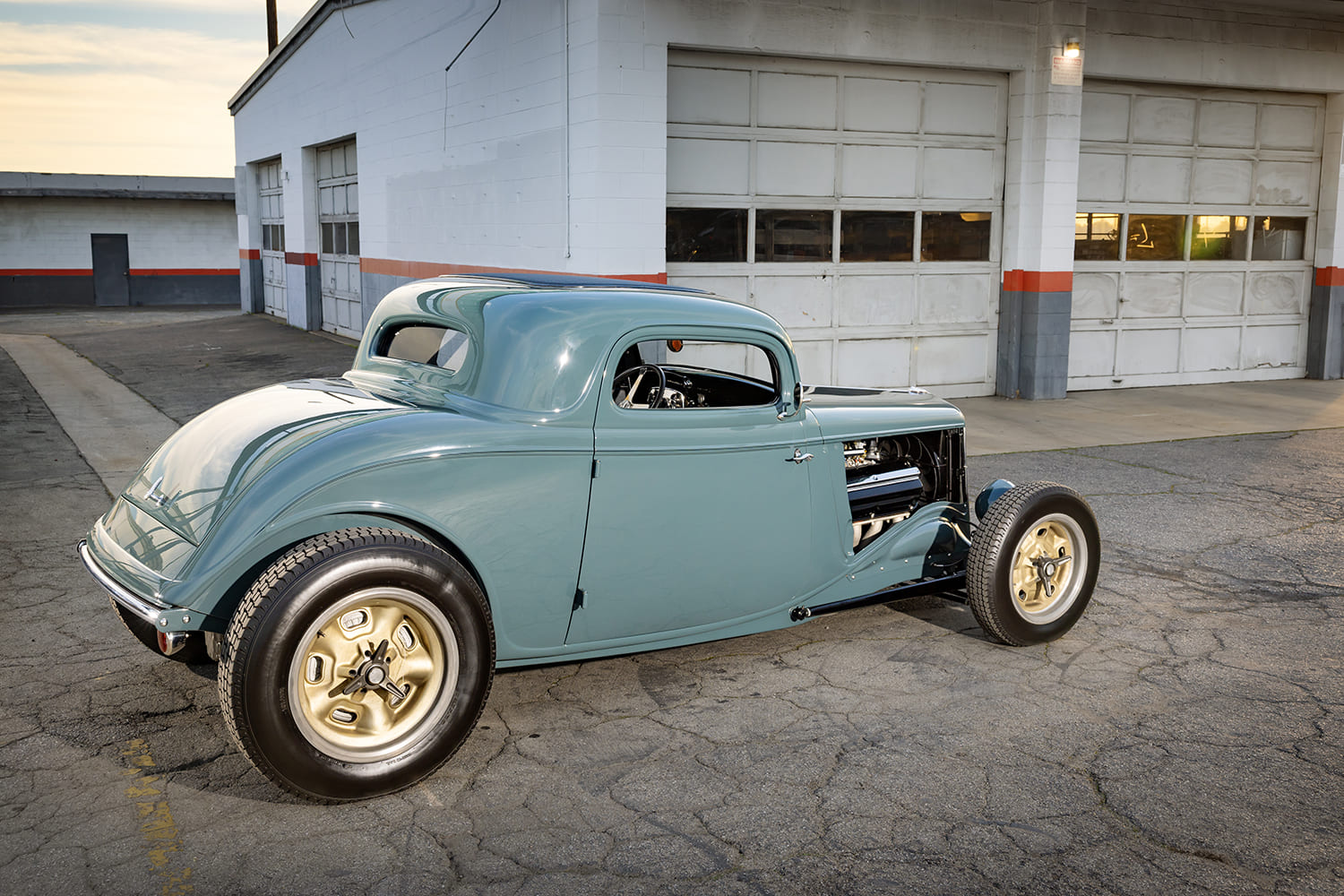 Rear three-quarter perspective of a chopped 1933 Ford Coupe showing the curved rear trunk decklid, large rear slicks, and custom paint finish.