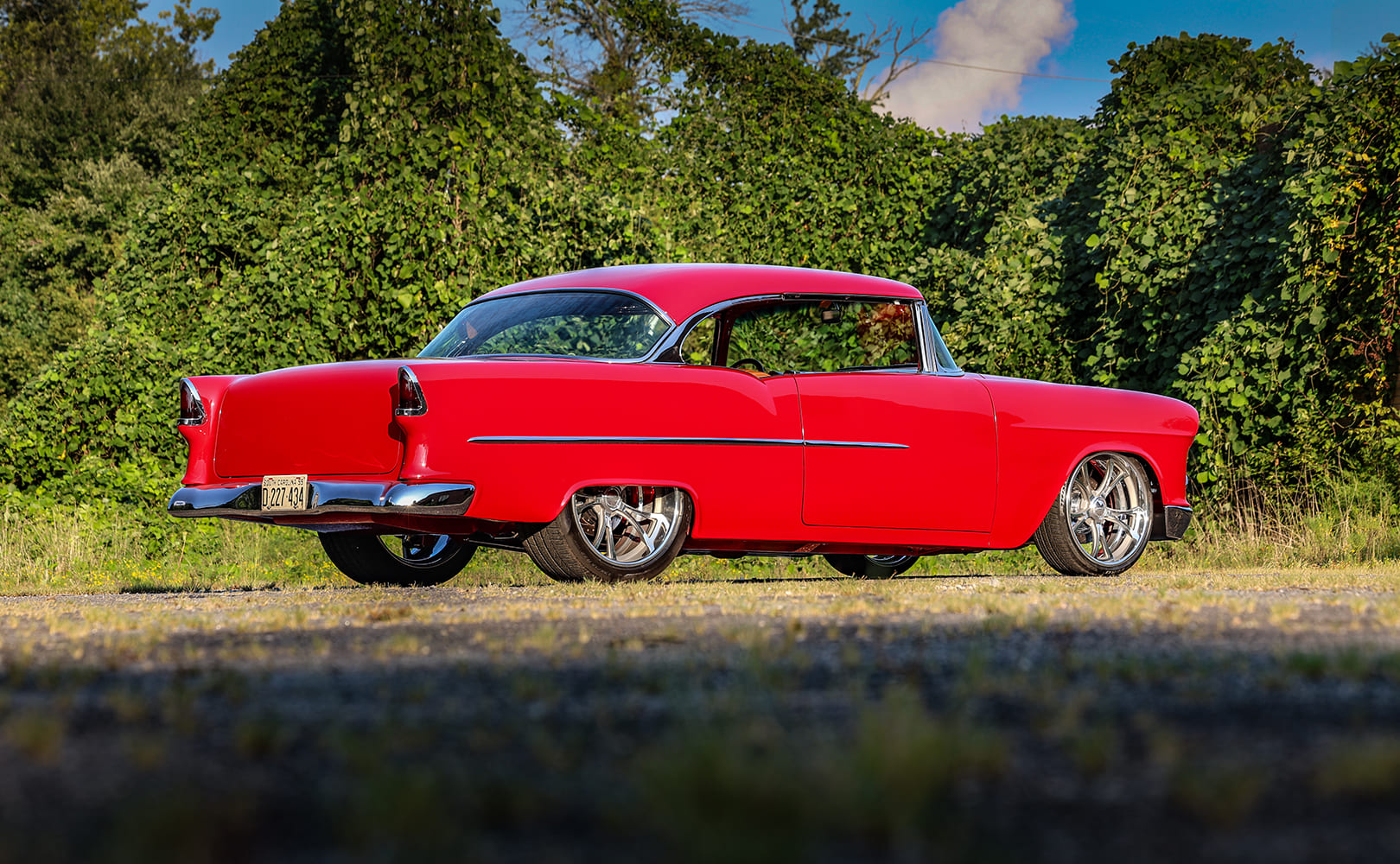 Low-angle rear profile of a red 1955 Chevrolet Bel Air restomod with smoothed bodywork and polished chrome rear bumper.