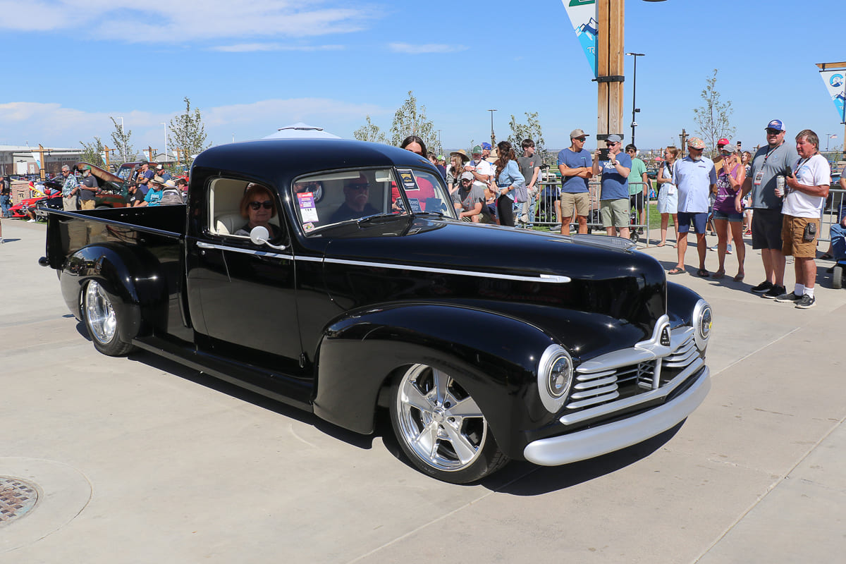 Driver with mustache and sunglasses seated in a classic black hot rod truck holding out his Modern Rodding Magazine Goodguys Award plaque.