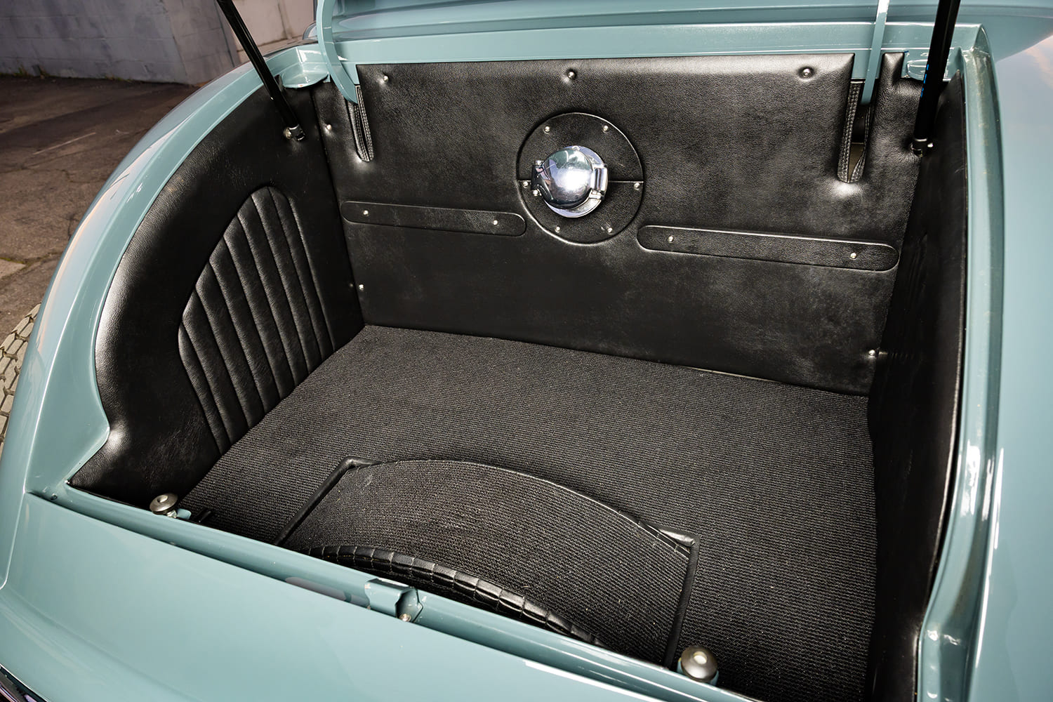 Open rear trunk compartment of a 1933 Ford street rod finished in pleated black leather upholstery with a polished center gas filler cap.
