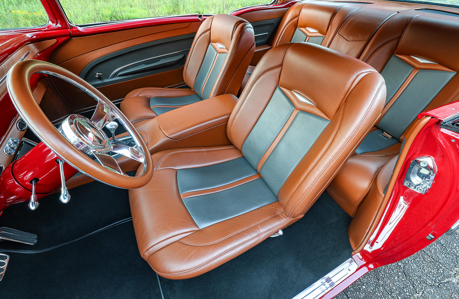 Overhead view into the custom leather cabin of a red 1955 Bel Air showing front bucket seats, rear bench, and full center console.