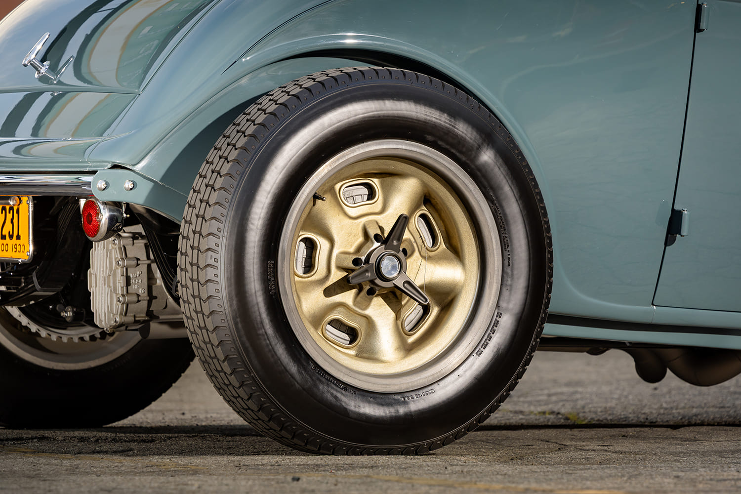 Close-up of a vintage kidney-bean gold wheel with a knock-off spinner and massive rear tire mounted on a custom 1933 Ford Coupe.