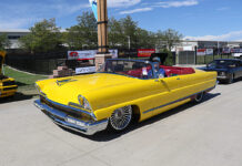 Front three-quarter high angle of a bright yellow custom 1956 Lincoln convertible with red leather interior and wire spoke wheels cruising the grounds