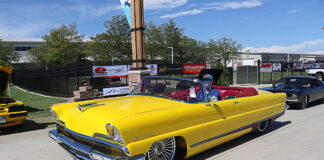 Front three-quarter high angle of a bright yellow custom 1956 Lincoln convertible with red leather interior and wire spoke wheels cruising the grounds