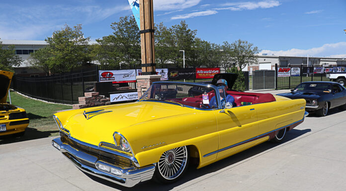 Goodguys Loveland – 28th Griot’s Garage Colorado Nationals Front three-quarter high angle of a bright yellow custom 1956 Lincoln convertible with red leather interior and wire spoke wheels cruising the grounds
