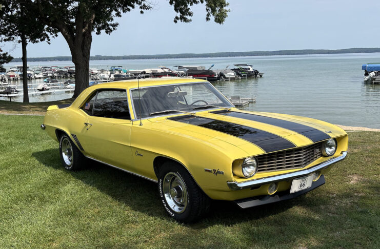 Front three-quarter view of a Daytona Yellow 1969 Chevy Camaro Z28 with black racing stripes parked by a lake.