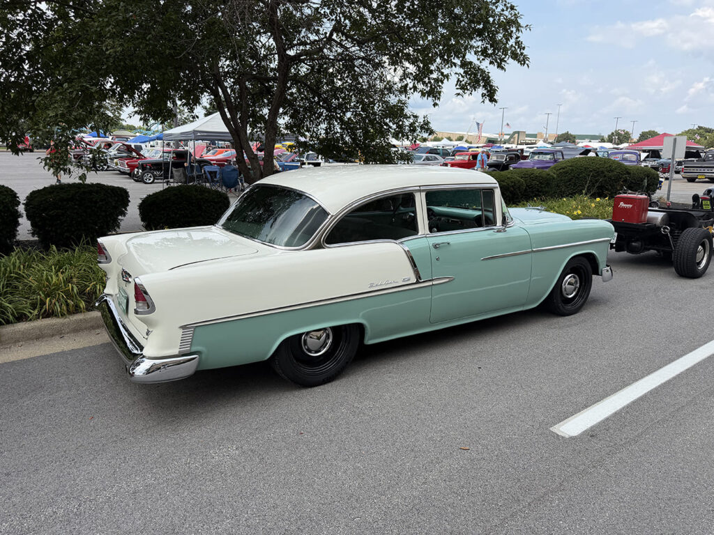 Rear three-quarter perspective of a classic seafoam green and white two-tone 1955 Chevrolet two-door post sedan parked outdoors with color-matched steel wheels.