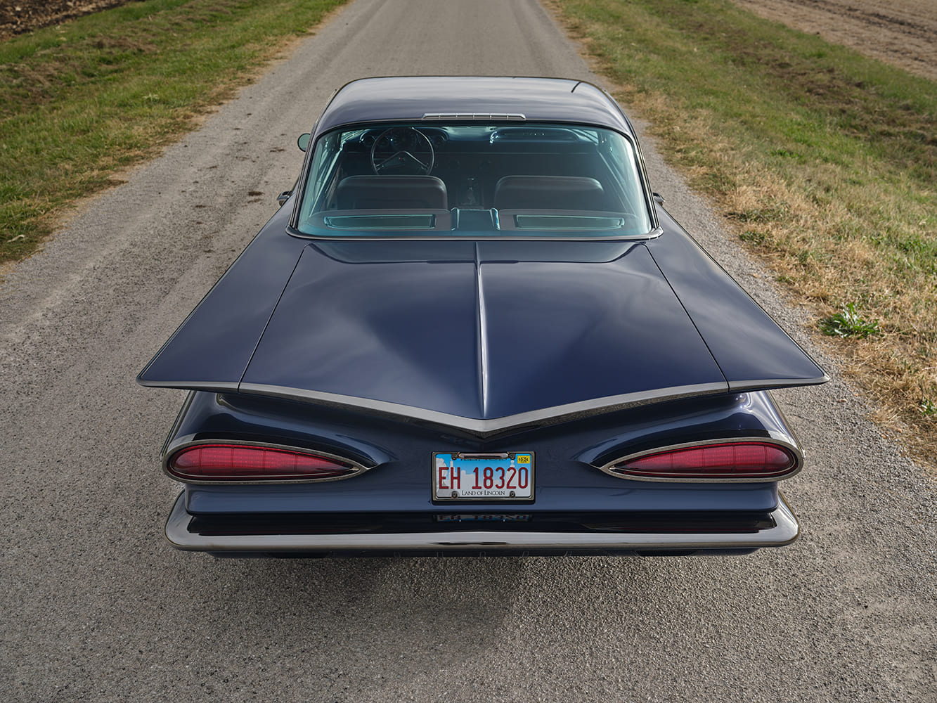 1959 Chevrolet Impala rear centered view iconic batwing fins taillights blue custom coupe rural setting