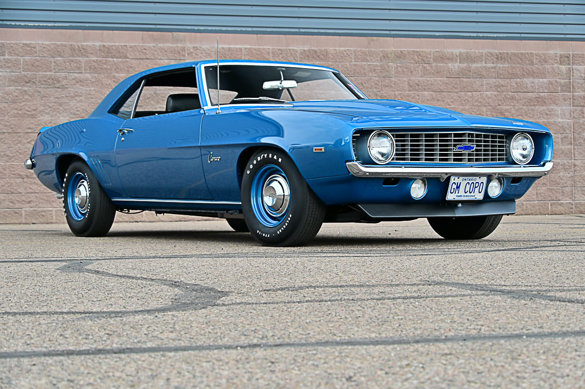 Low front three-quarter angle of a Le Mans Blue 1969 Chevrolet Camaro coupe fitted with color-matched steel wheels, dog-dish caps, and GM COPO license plate.