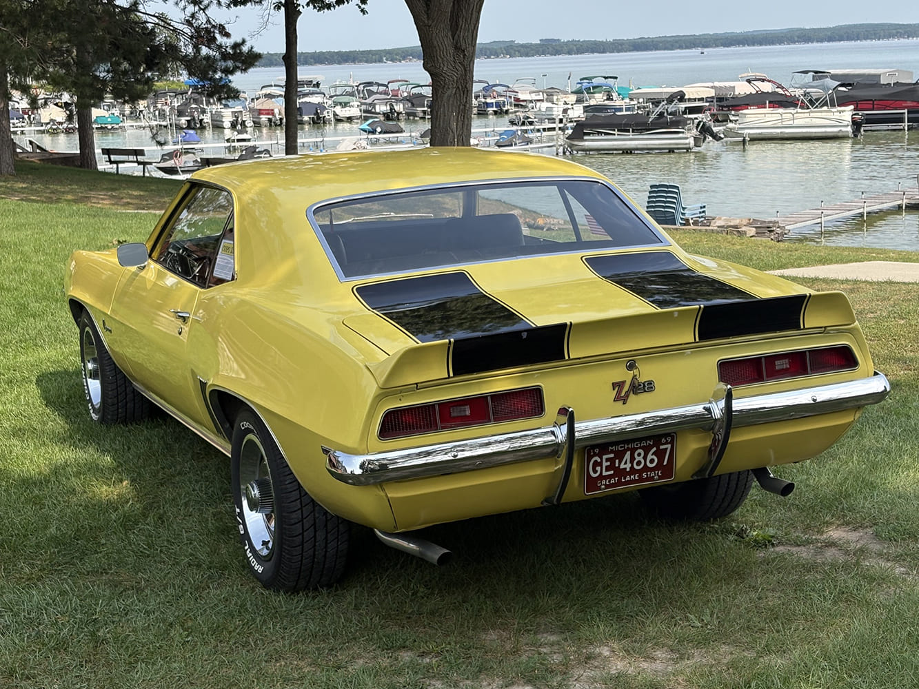 Rear view of a yellow 1969 Chevrolet Camaro Z28 showing rear spoiler, black decklid stripes, chrome bumper, and dual exhaust.