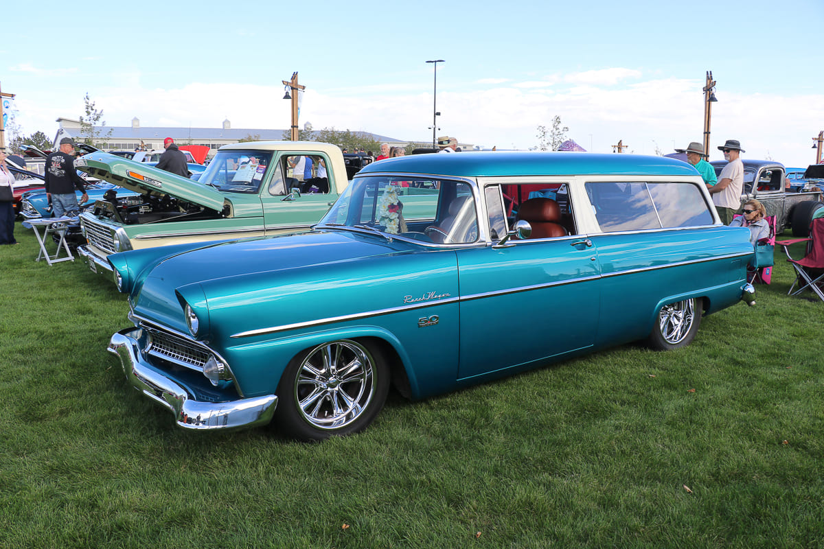 Side three-quarter profile of a lowered metallic teal and white two-tone 1954 Ford Ranch Wagon parked on showfield grass.