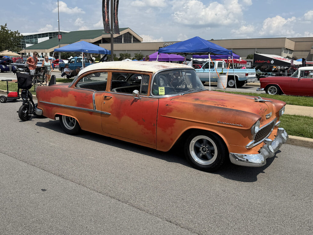 Front three-quarter view of a lowered two-tone patina orange and white 1955 Chevrolet 210 sedan sitting on gray Torq Thrust-style wheels.