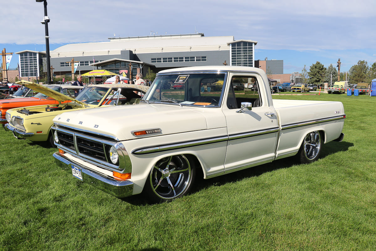 Front three-quarter angle of a classic cream-white 1970 Ford F-100 pickup truck with modern chrome wheels parked at an outdoor car meet.