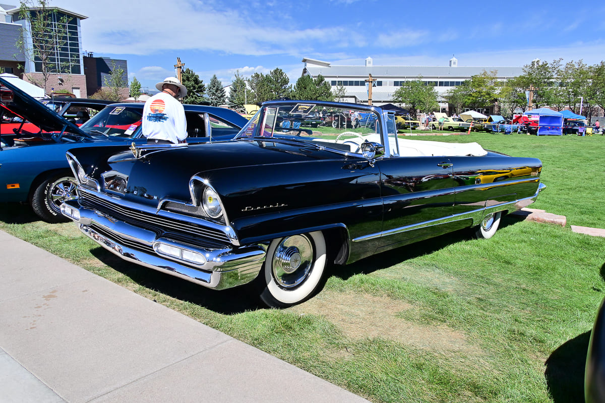 Low-angle front three-quarter view of a glossy black 1956 Lincoln Premiere convertible with white interior and wide whitewall tires on a show field.