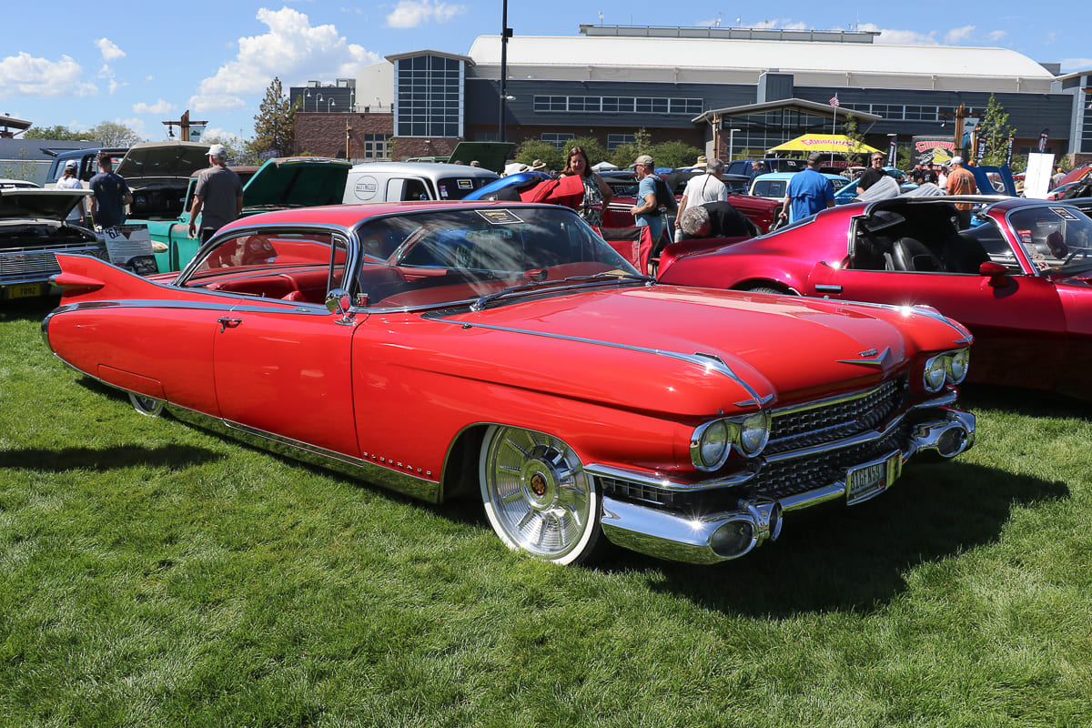 Front three-quarter perspective of a bright red 1959 Cadillac Eldorado featuring huge tail fins, dual chrome bullet bumpers, and modern billet wheels on grass.