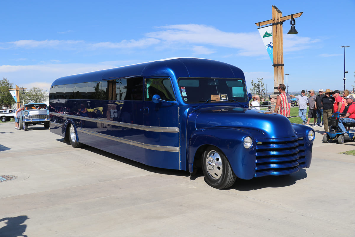 Low front three-quarter view of a massive, slammed royal blue vintage Chevy COE streamliner coach bus cruising the grounds at Goodguys Colorado Nationals.
