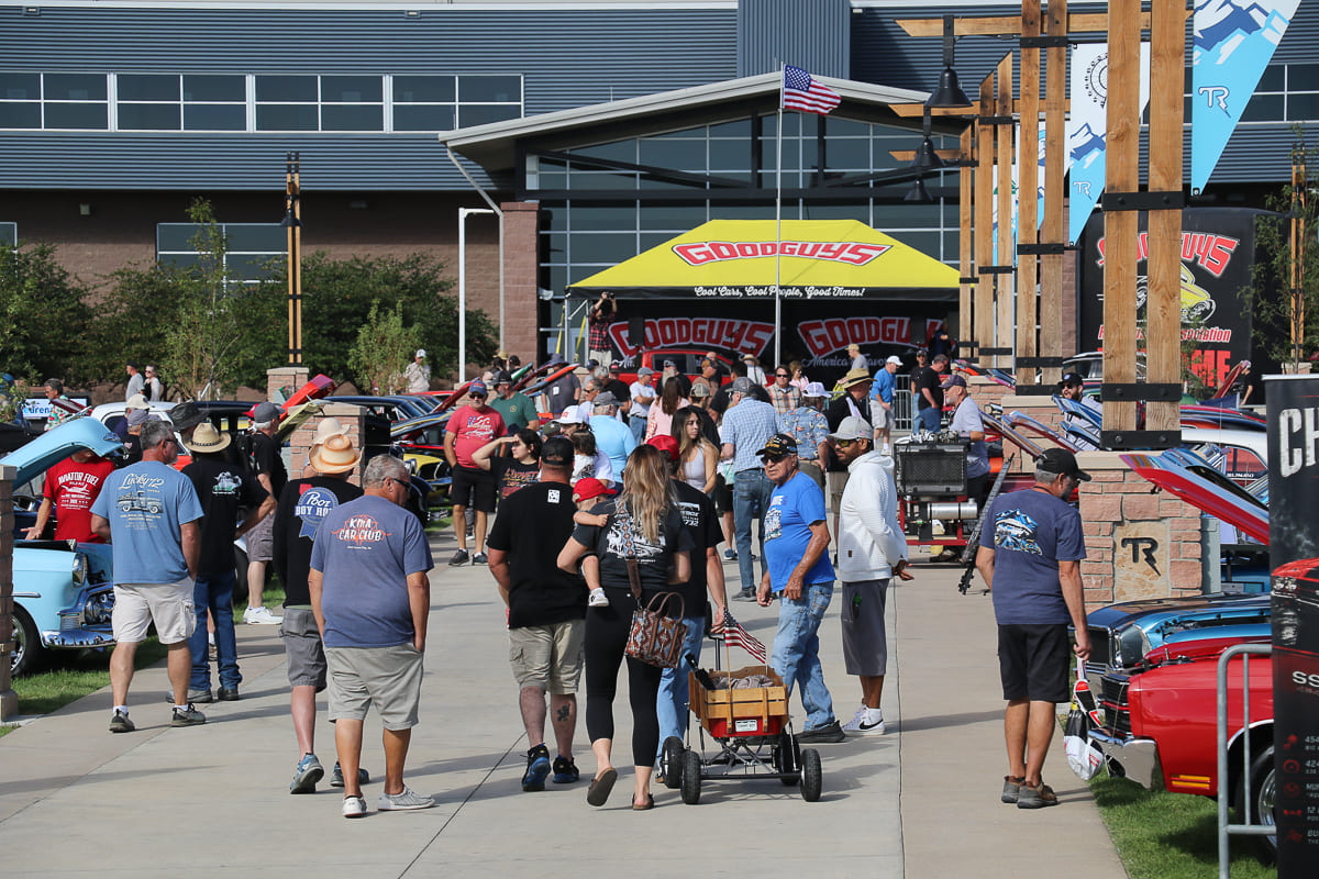 Large crowd of spectators walking along an event concourse toward the yellow Good Guys stage and exhibition facility entrance.