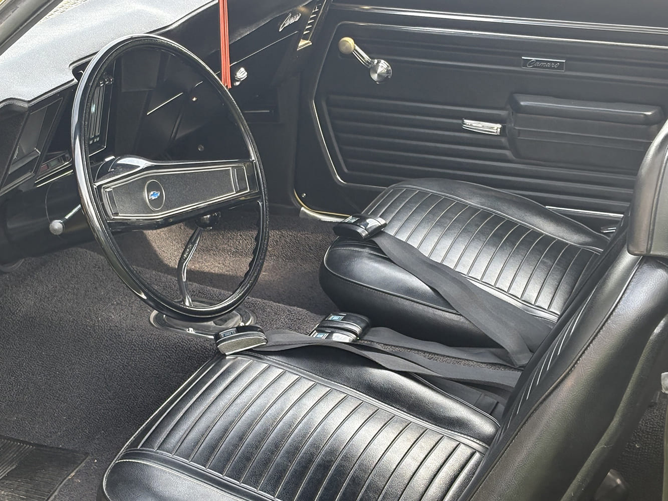 Interior driver view of a 1969 Camaro Z28 featuring black vinyl bucket seats, factory lap belts, and two-spoke steering wheel.