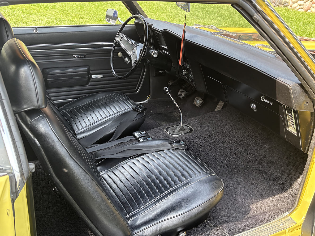 Full cabin view of a 1969 Chevy Camaro interior showing black vinyl upholstery, dashboard, and floor-mounted manual 4-speed shifter.