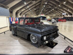 2026 Grand National Truck Show Front three-quarter view of the dark gray metallic 1963 Chevrolet C10 custom pickup "50 SHDZE" displayed on elevated stands over faux wood flooring.