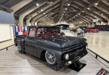 2026 Grand National Truck Show Front three-quarter view of the dark gray metallic 1963 Chevrolet C10 custom pickup "50 SHDZE" displayed on elevated stands over faux wood flooring.