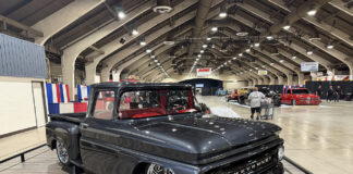 Front three-quarter view of the dark gray metallic 1963 Chevrolet C10 custom pickup "50 SHDZE" displayed on elevated stands over faux wood flooring.