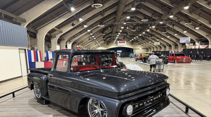 2026 Grand National Truck Show Front three-quarter view of the dark gray metallic 1963 Chevrolet C10 custom pickup "50 SHDZE" displayed on elevated stands over faux wood flooring.