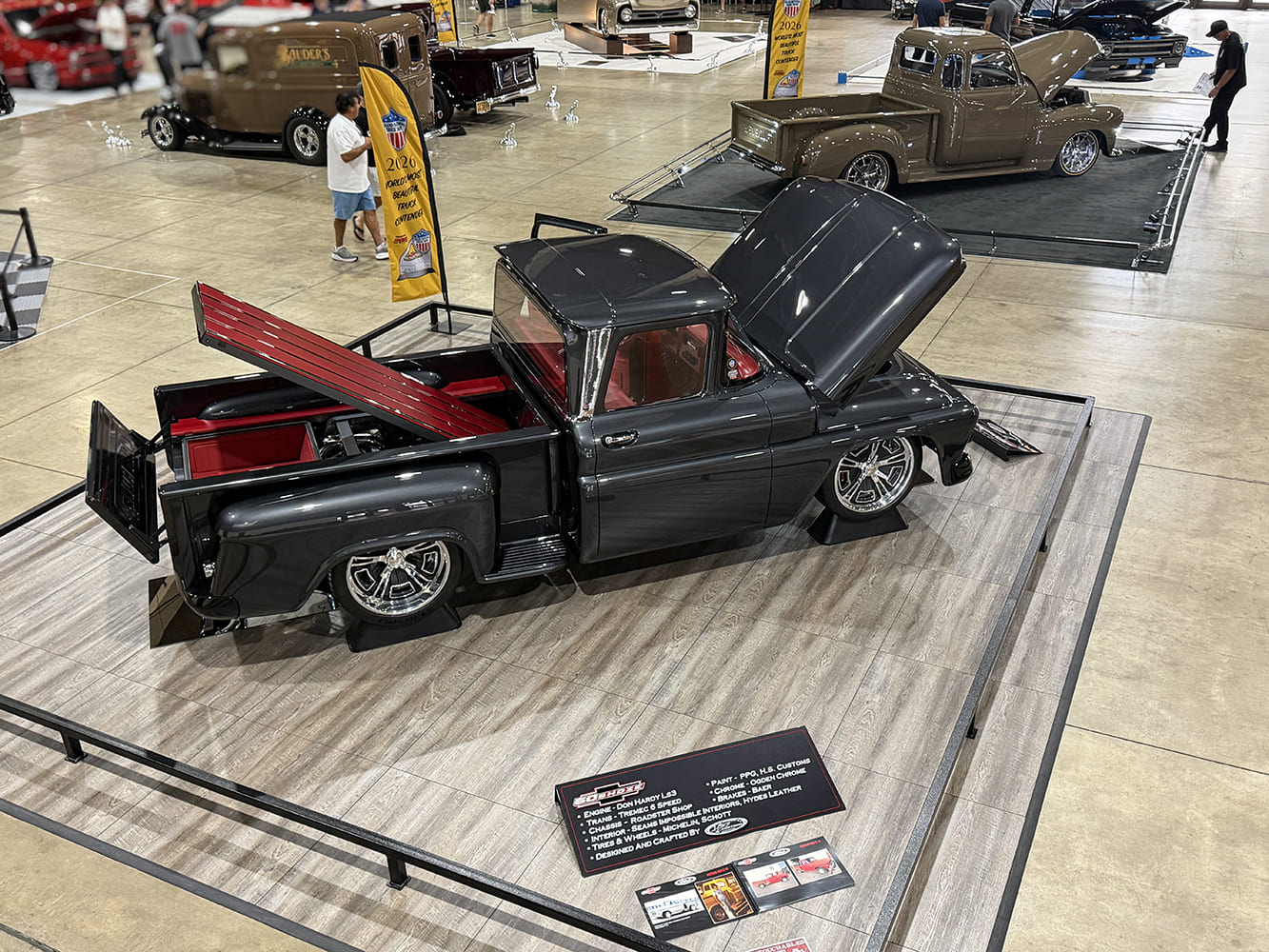 Elevated rear three-quarter view of the custom 1963 Chevy C10 with its hood propped and bed floor raised, accompanied by build specification boards.