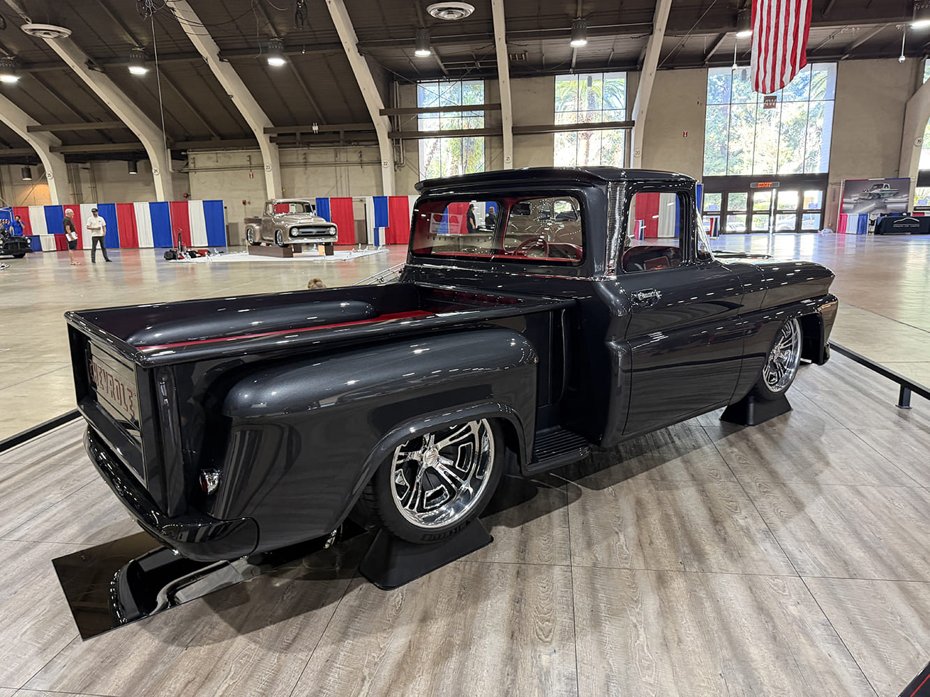 Rear three-quarter perspective of the gloss charcoal gray 1963 Chevy C10 custom stepside highlighting red bed accents and deep-dish polished wheels.