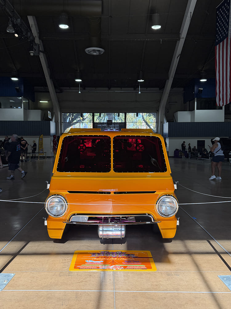 Direct front view of a vibrant yellow custom Dodge A100 cab-over pickup displayed inside Expo Hall at the Grand National Truck Show.
