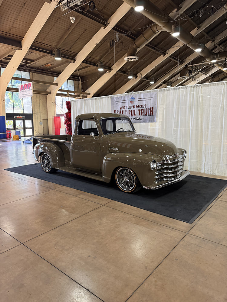 Front three-quarter perspective of a pristine tan metallic Chevrolet 3100 pickup truck with thin gold-stripe tires and chrome grille on display.