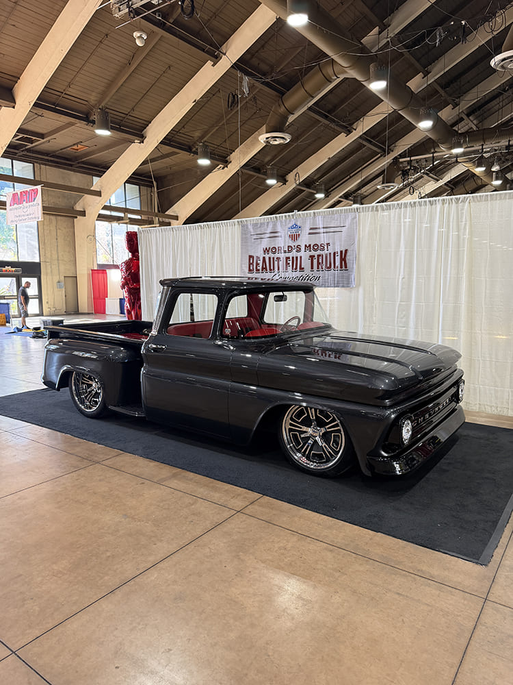 Low front three-quarter view of Gary and Stefanie Holyoak’s charcoal gray 1963 Chevy C10 stepside with red leather interior in front of event stage drapes.