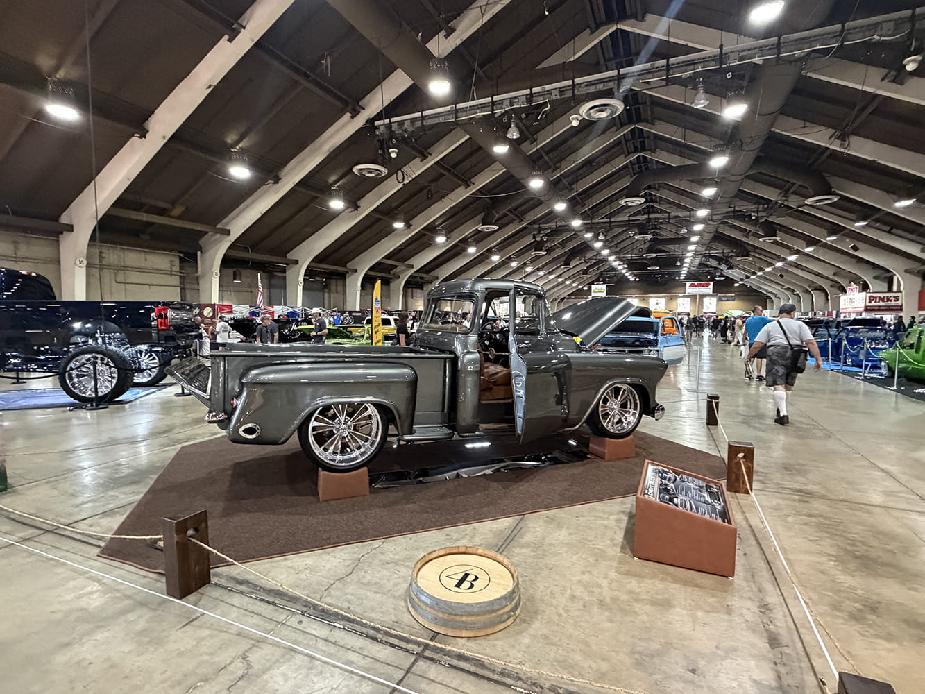 Rear three-quarter perspective of a custom dark metallic gray Chevrolet Task Force pickup elevated on display risers with matching decorative barrel and placard.