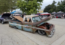 2026 Goodguys Columbus Nationals Trucks Front three-quarter angle of a slammed weathered Chevy C10 pickup with an open hood, raised wood bed floor, and chrome-rimmed wheels outdoors.