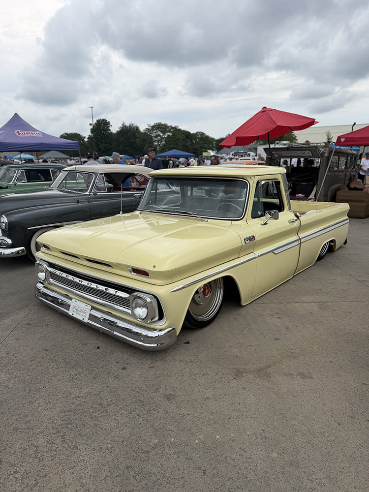 Low-angle front three-quarter view of a lowered pale yellow Chevrolet C10 fleetside pickup truck laid out low on polished solid wheels under an overcast sky at an outdoor car show.