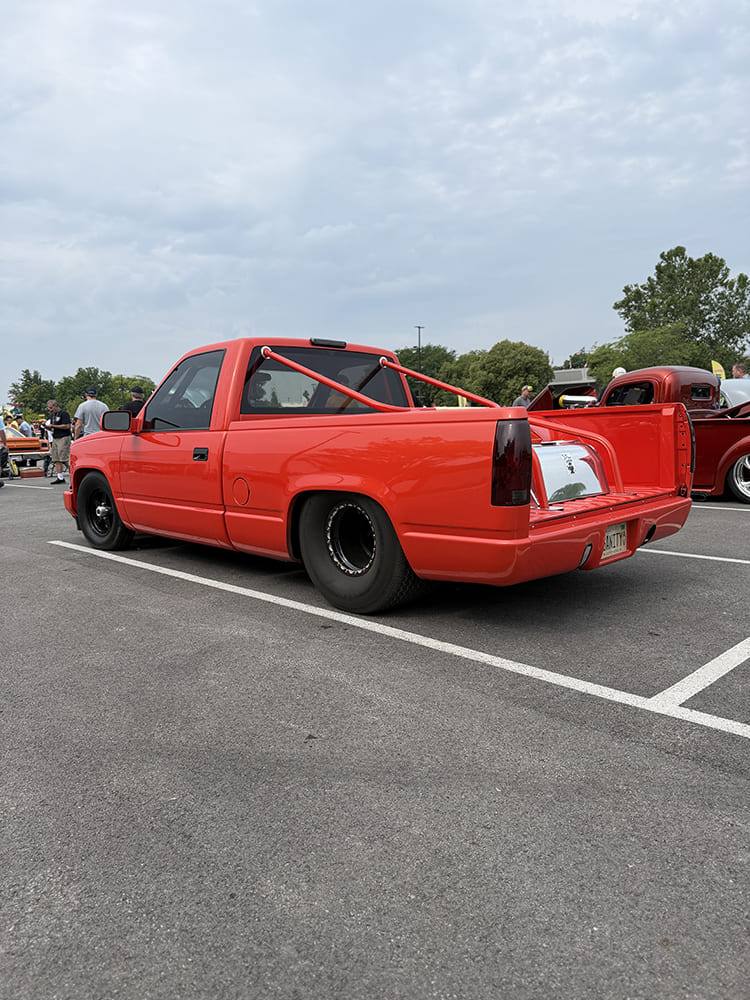 Rear three-quarter view of a bright red Chevy OBS pickup showing wide Mickey Thompson rear drag slicks, beadlock wheels, custom bed roll bar, and polished fuel cell.