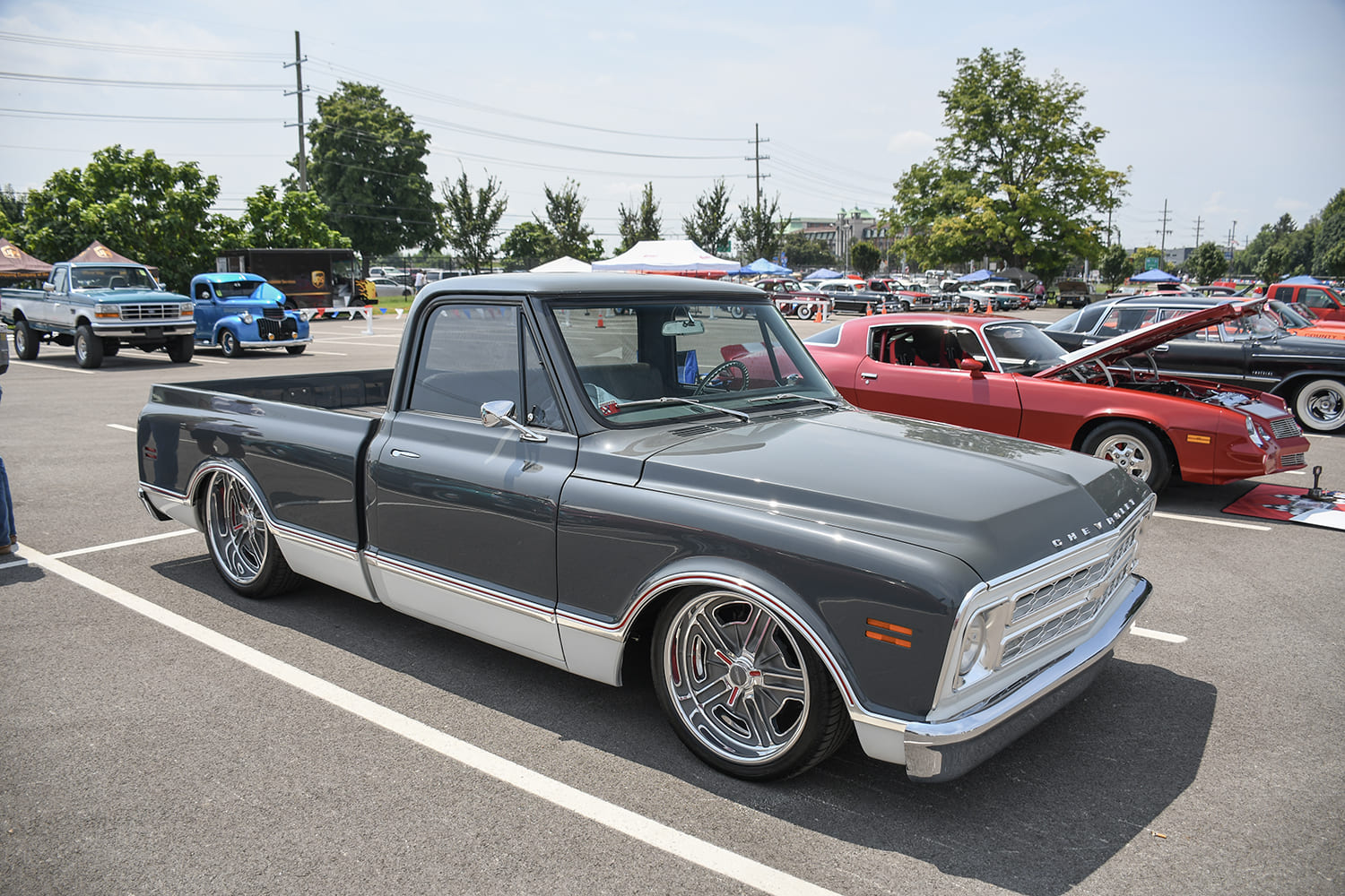 Front three-quarter parking lot perspective of a lowered dark metallic gray Chevrolet C10 pickup with white lower body trim and polished five-spoke wheels.