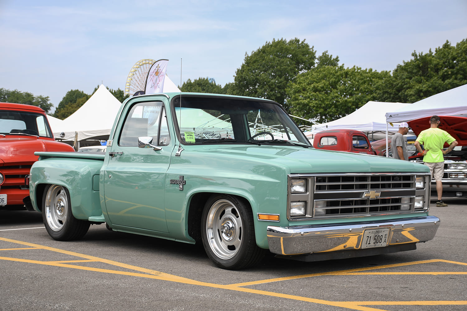 Front three-quarter low-angle view of a lowered seafoam mint green Chevrolet C10 Silverado stepside pickup on polished rally-style wheels.