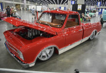 Classic Truck Action at the 2026 NSRA Street Rod Nationals Front three-quarter high angle of a slammed candy red Chevrolet C10 pickup with an open hood showcasing an eight-stack velocity stack engine and chrome wheels inside the expo center.