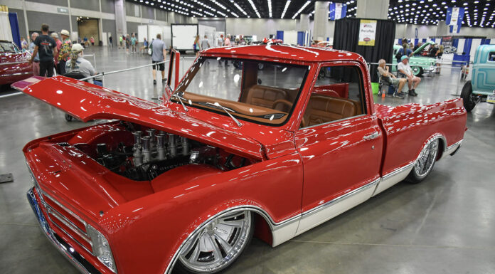 Classic Truck Action at the 2026 NSRA Street Rod Nationals Front three-quarter high angle of a slammed candy red Chevrolet C10 pickup with an open hood showcasing an eight-stack velocity stack engine and chrome wheels inside the expo center.